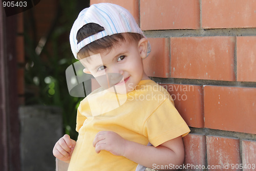 Image of Little boy in yellow shirt at brick wall