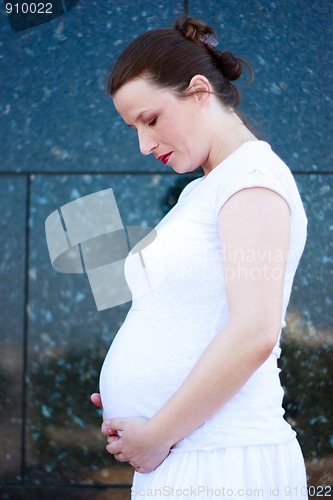 Image of Beautiful young pregnant girl looking at her belly