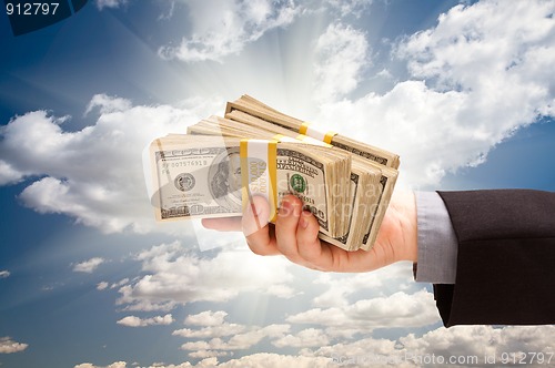 Image of Male Hand Holding Stack of Cash Over Clouds and Sky