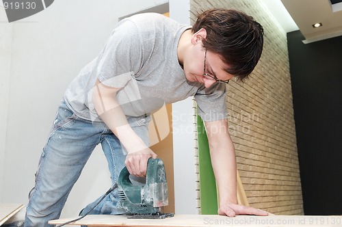 Image of worker cutting floor board with jigsaw 