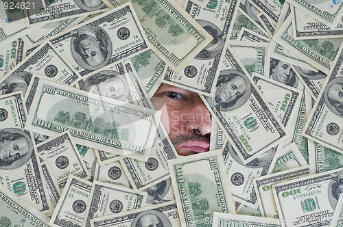 Image of man looking through a hole between dollar bills