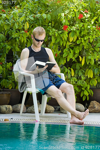Image of young man reading nearby the swimming pool