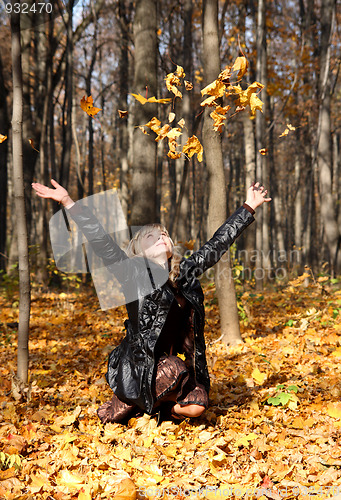 Image of beautiful girl throwing up autumn leaves