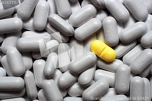 Image of one yellow pill on gray pills