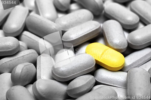 Image of one yellow pill on gray pills