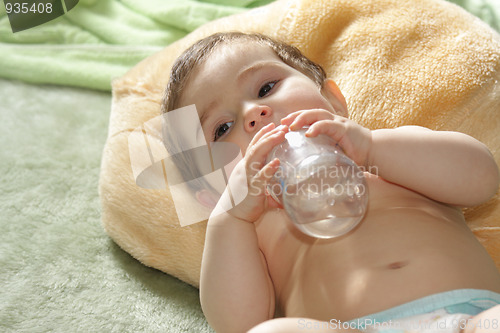 Image of Baby with bottle laying on rug