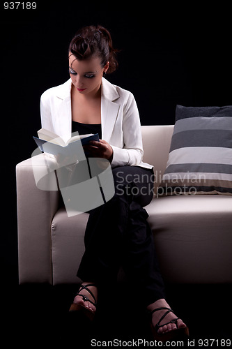 Image of Beautiful woman seated on couch reading a book