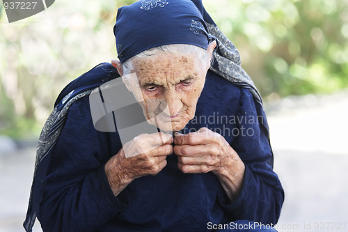 Image of Elderly woman buttoning dress up
