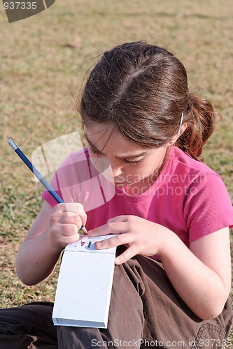 Image of Cute little girl with pigtails writes outdoor 