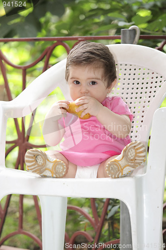 Image of Baby girl in pink eating pear