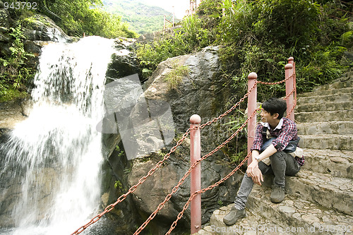 Image of chinese man sitting on the stair in the forest and looking at th