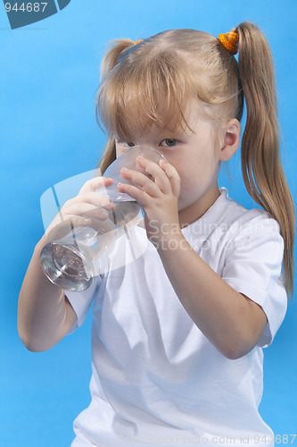 Image of Small cute girl is drinking water on blue background