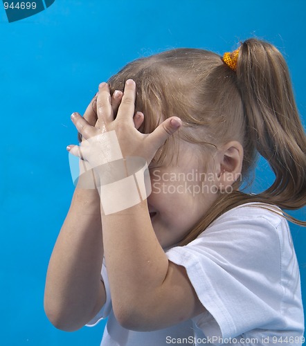 Image of Small girl is covering her face by hands isolated on blue