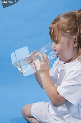 Image of Small cute girl is drinking water on blue background