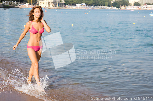 Image of Dark-haired girl in a swimsuit walking on the beach