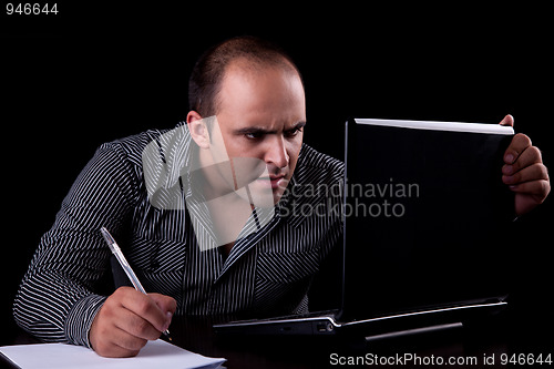 Image of surprised businessman looking to computer and taking notes