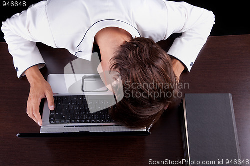 Image of Tired young businessman with head on the computer 