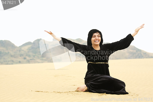 Image of Happy woman in shawl sitting on sand