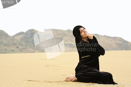 Image of Woman in shawl sitting on sand looking up