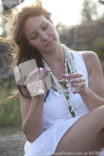 Image of Attractive woman applying nail polish outdoors.