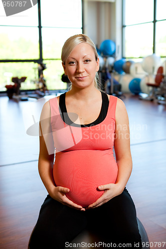 Image of Pregnant woman sitting on fitness ball holding belly.