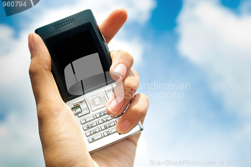 Image of Mobile phone in hand over blue sky background.