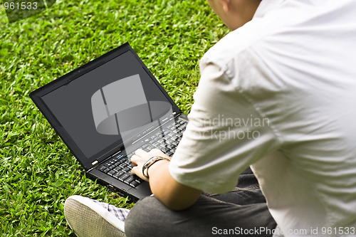 Image of Man siting on the grass using laptop 