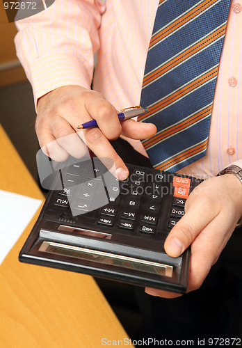 Image of businessman counts money on calculator