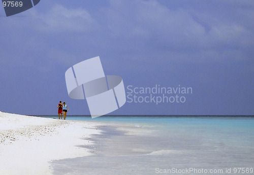 Image of man and woman walking trough white sand tropical beach