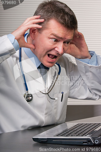 Image of Doctor gestures in despair at information on laptop