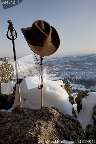 Image of trekking poles and hat in mountain scenery