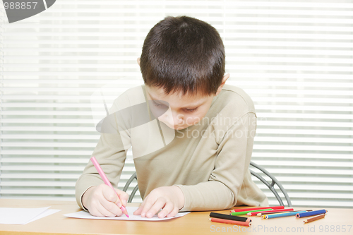 Image of Cute boy at desk drawing with crayons