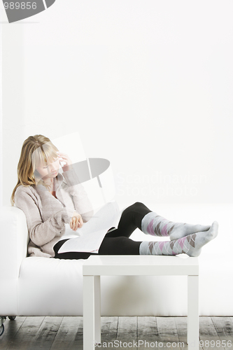 Image of Woman with cellphone and magazine laying on sofa