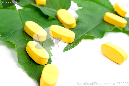 Image of yellow vitamin pills over green leaves