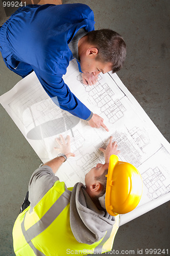Image of Builders talk about blueprint on bench