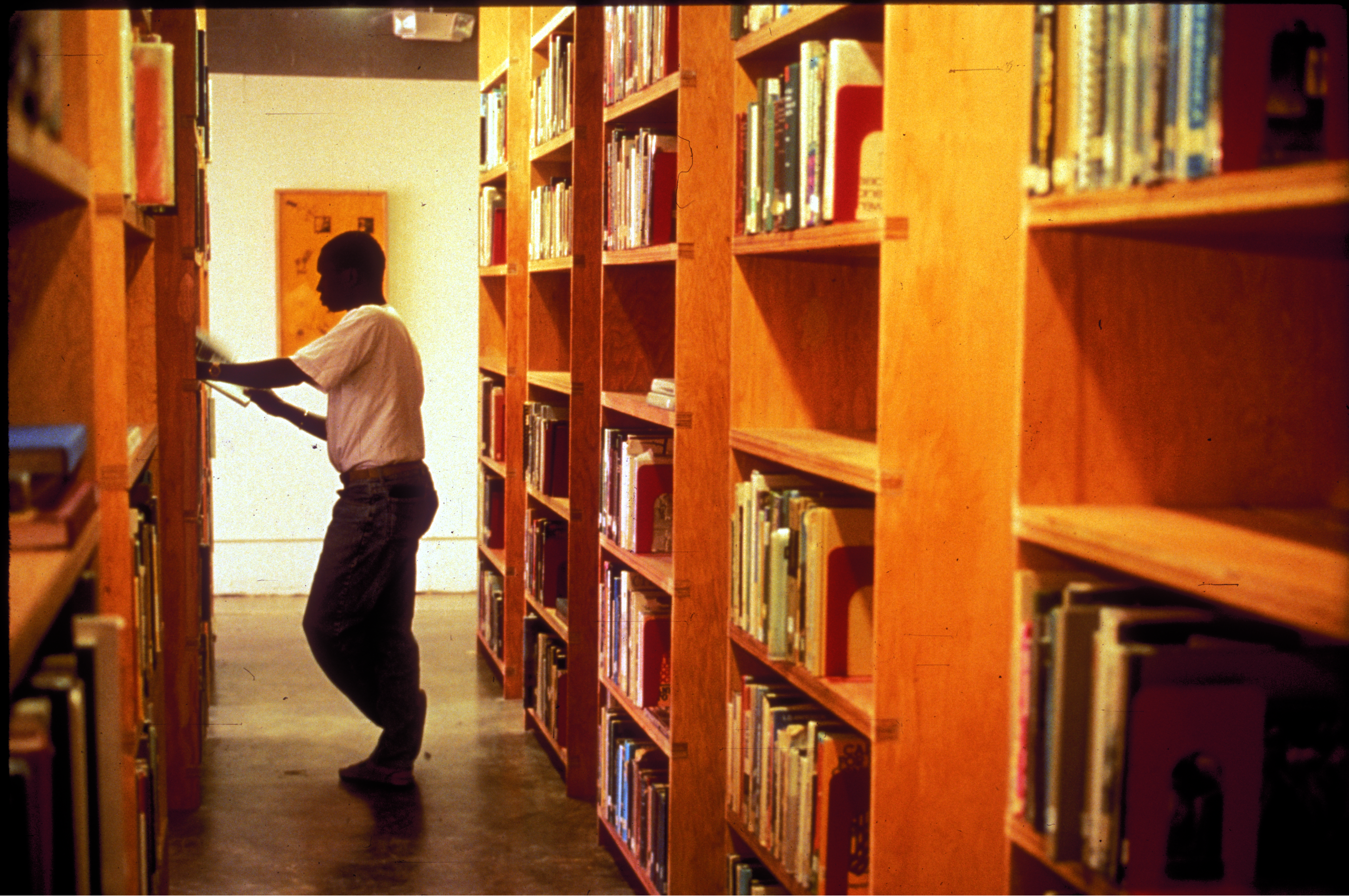 standing man reads book at bookshelf