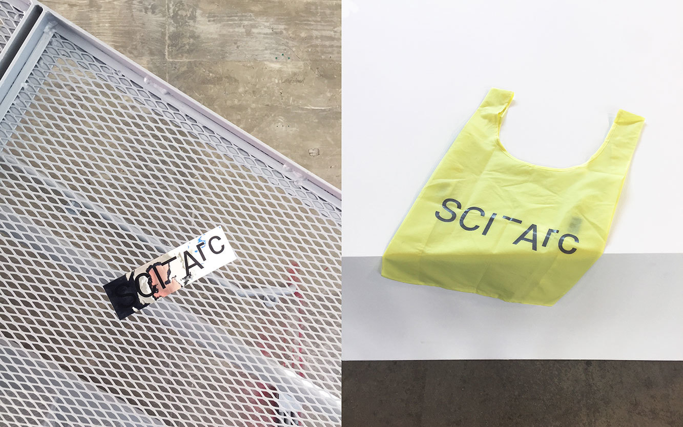 SCI-Arc silver sticker on metal scaffolding and a neon SCI-Arc bag on a table edge