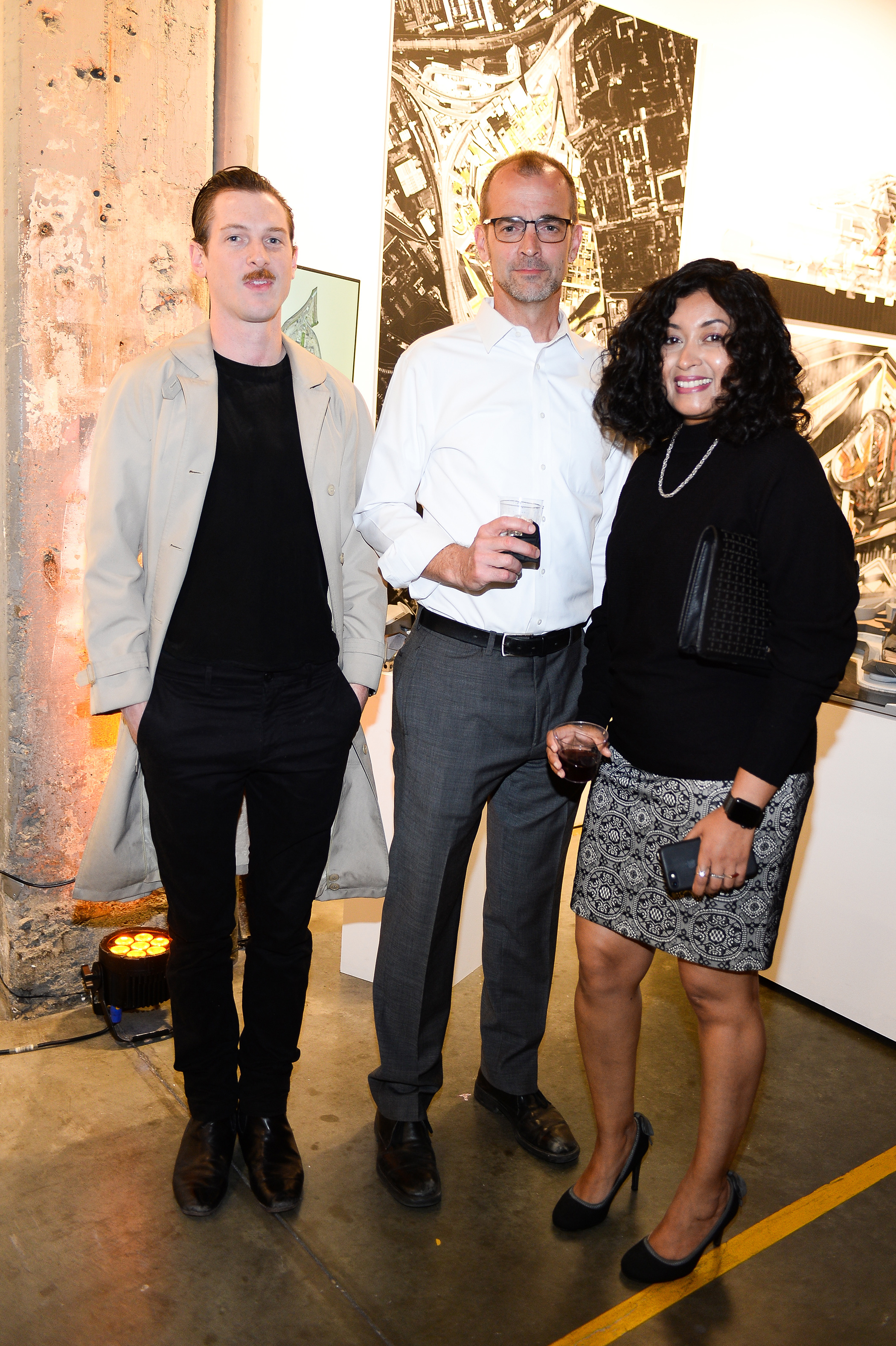 Two men and a woman stand and pose for a photo together.