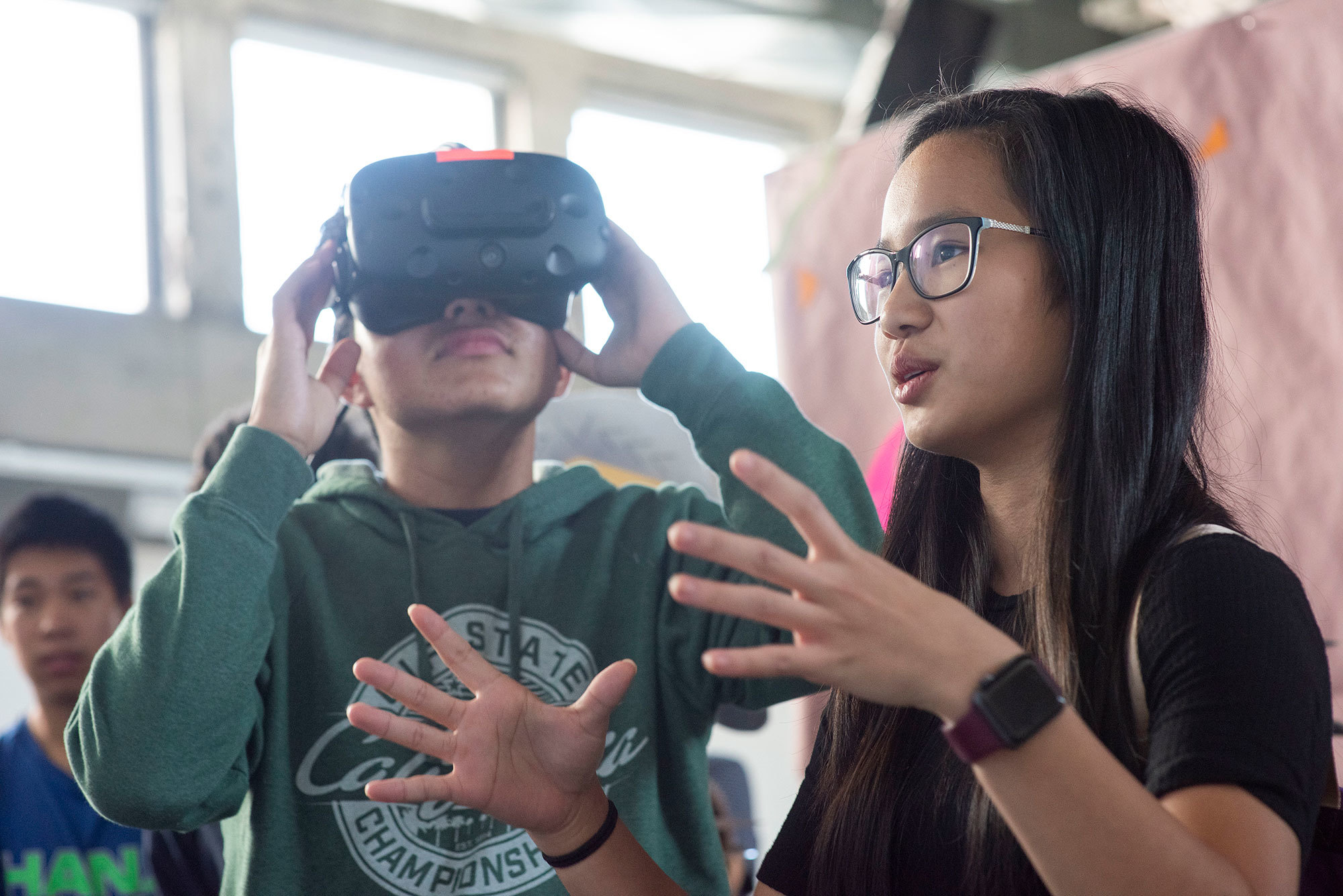 A high school participant explaining her project and a boy trying VR experience behind