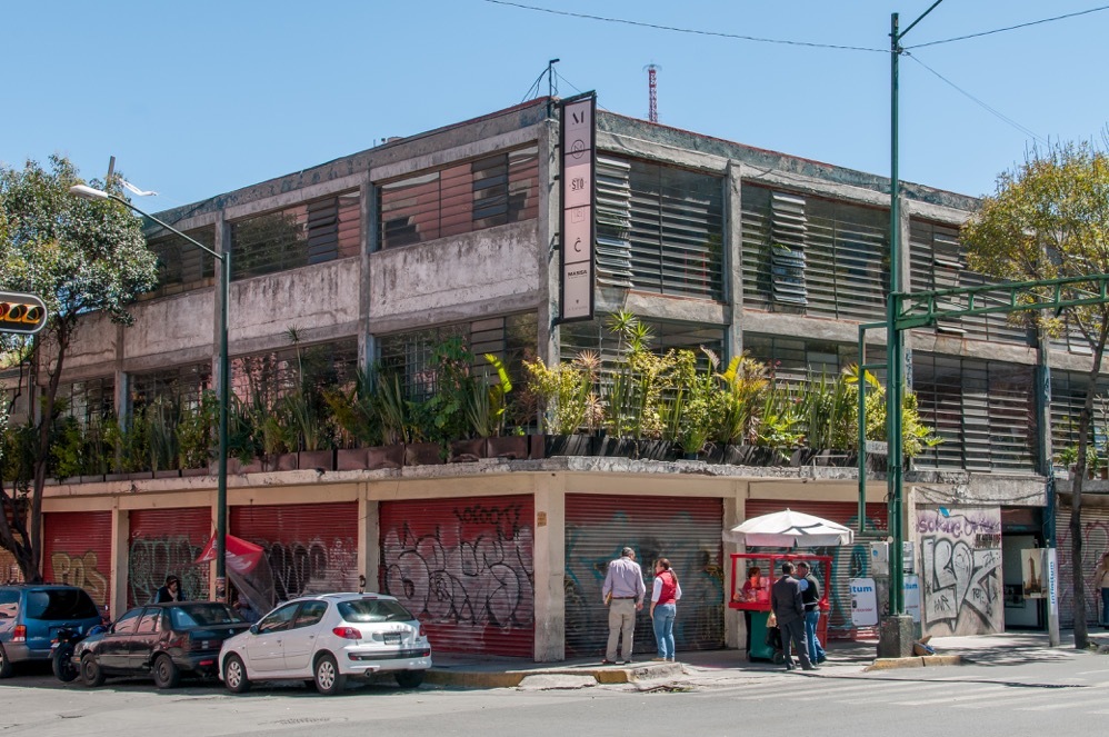 an old concrete building with potted palnts on second floor and graffiti on the walls