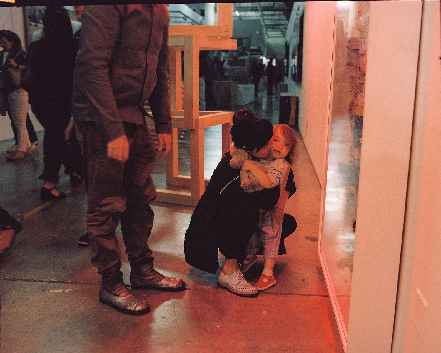 dark haired woman in dark clothing sitting and holding a child on a concrete floor with warm lighting next to a man