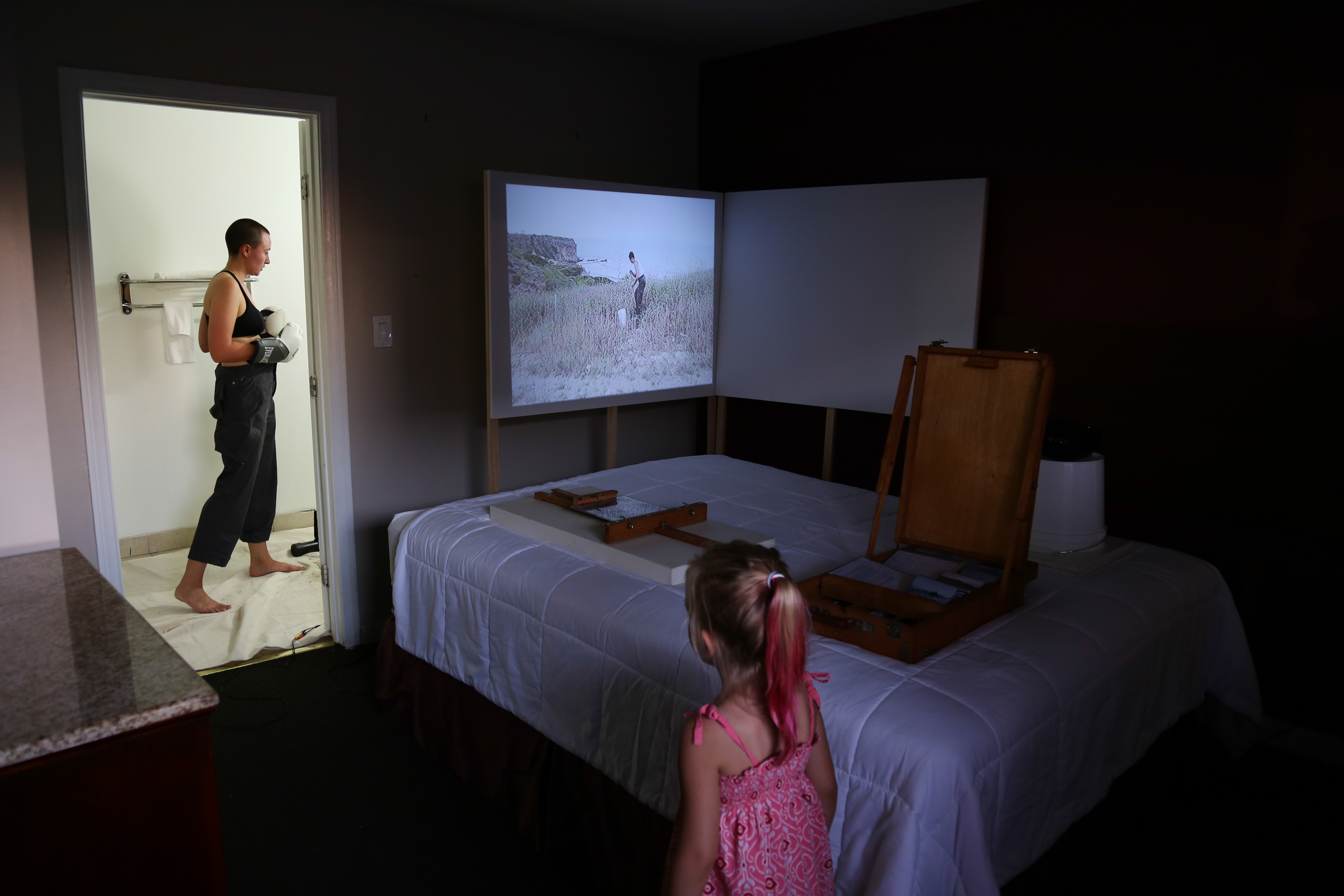 a dark room with a bed in corner with a little girl and a lady in boxing gloves