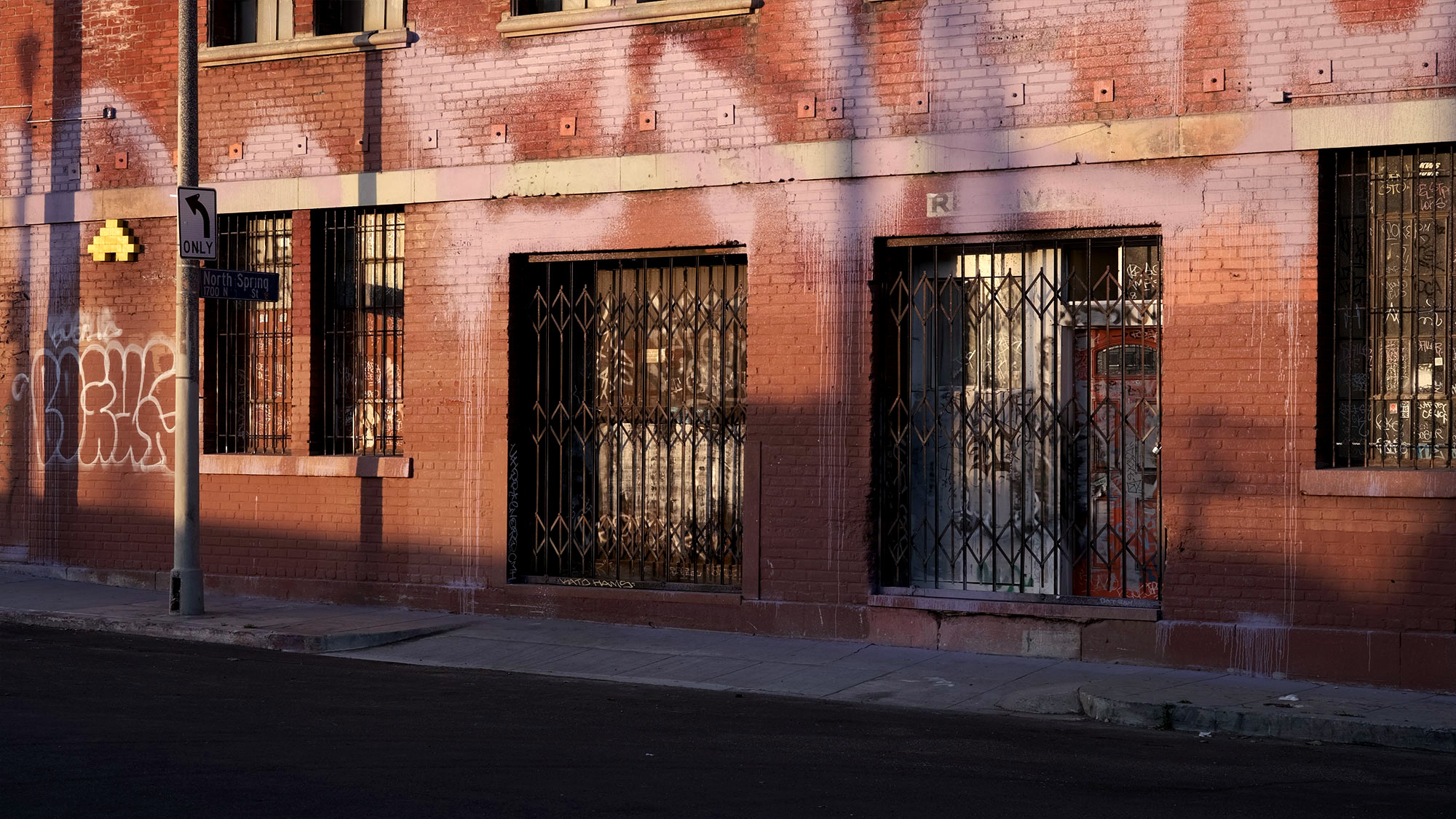 orange brick building with big pink text graffiti all over with metal screen doors in downtown of a big city