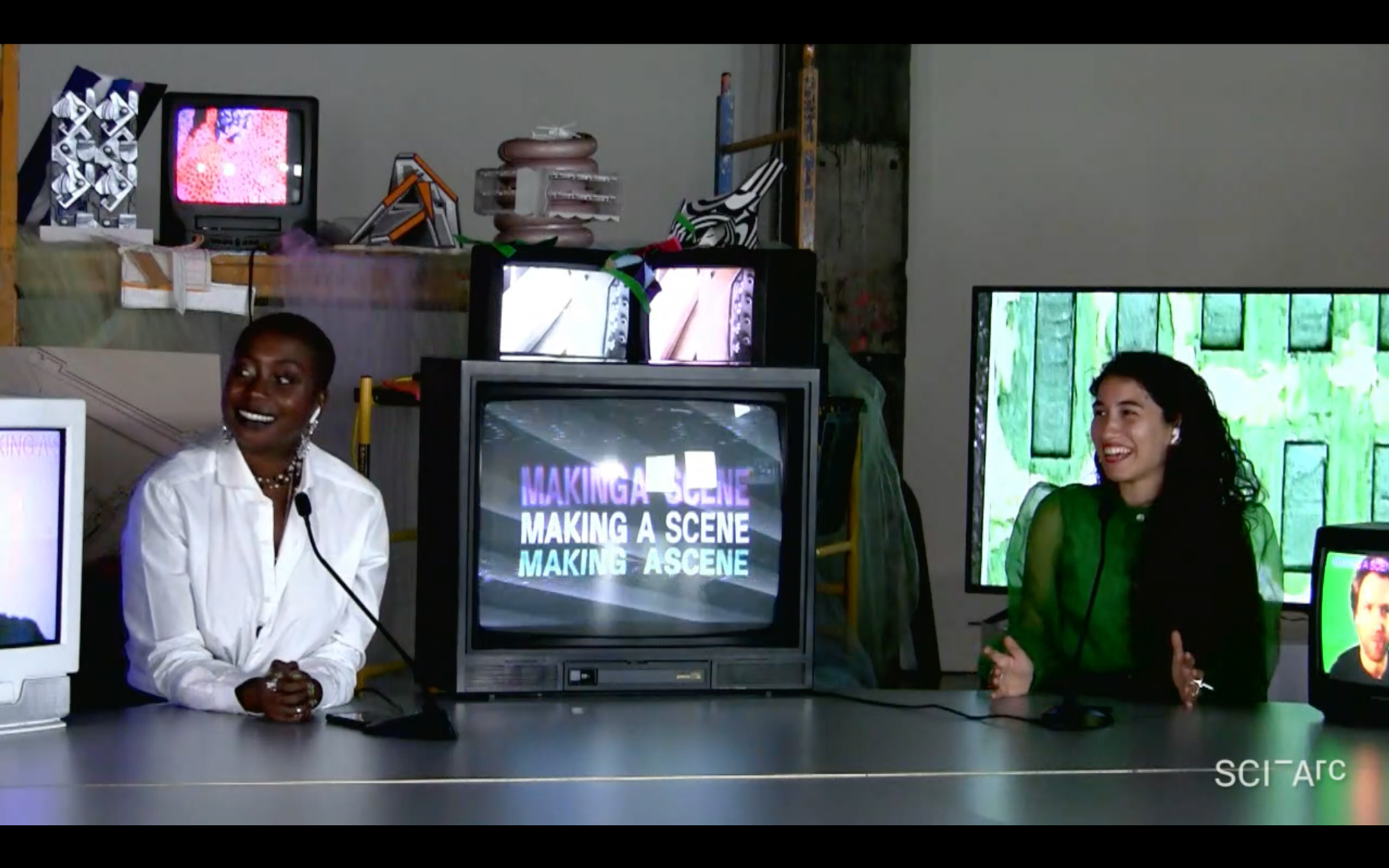 women smiling sitting between tv screens