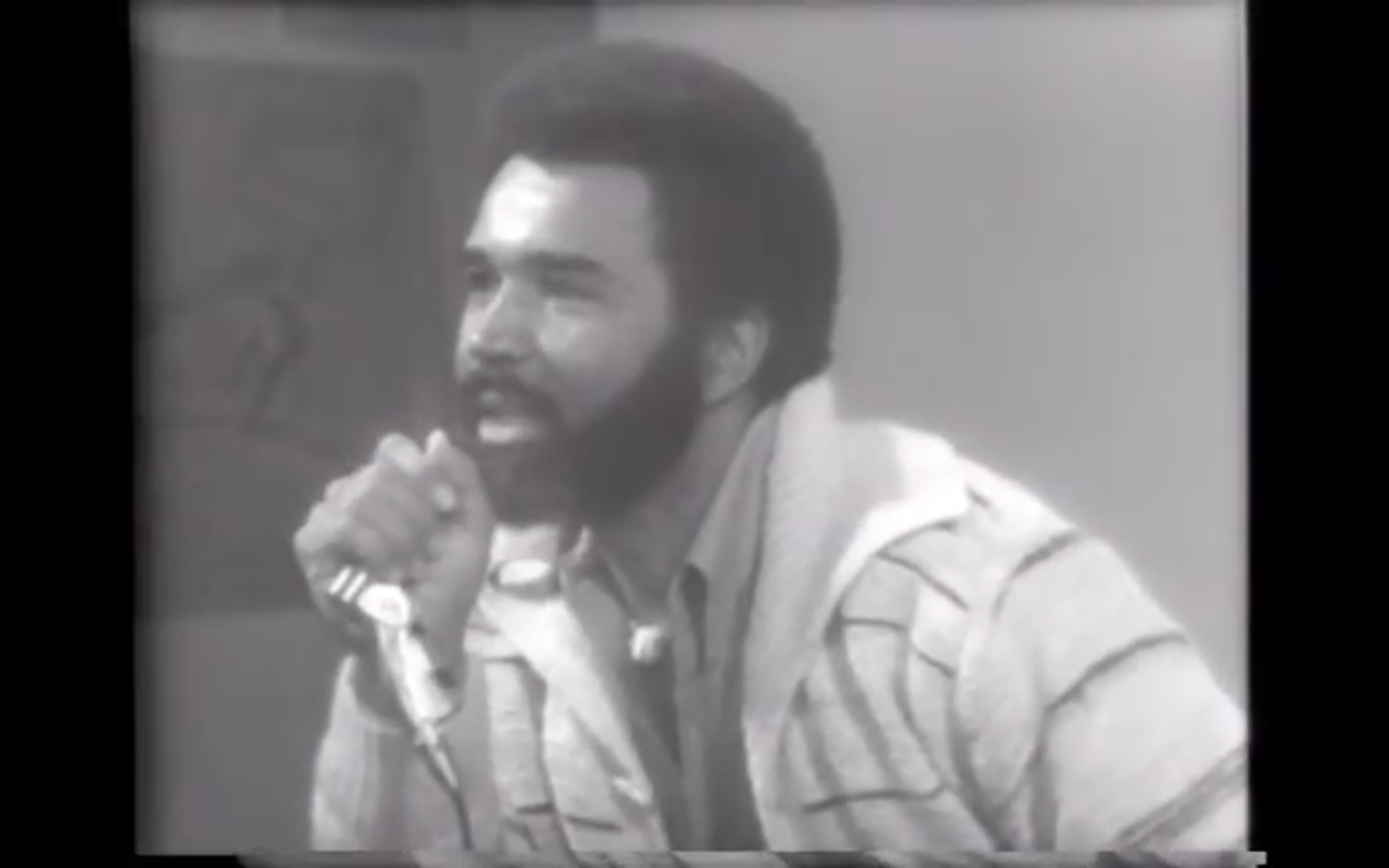black and white image of man in the 1970s speaking into microphone
