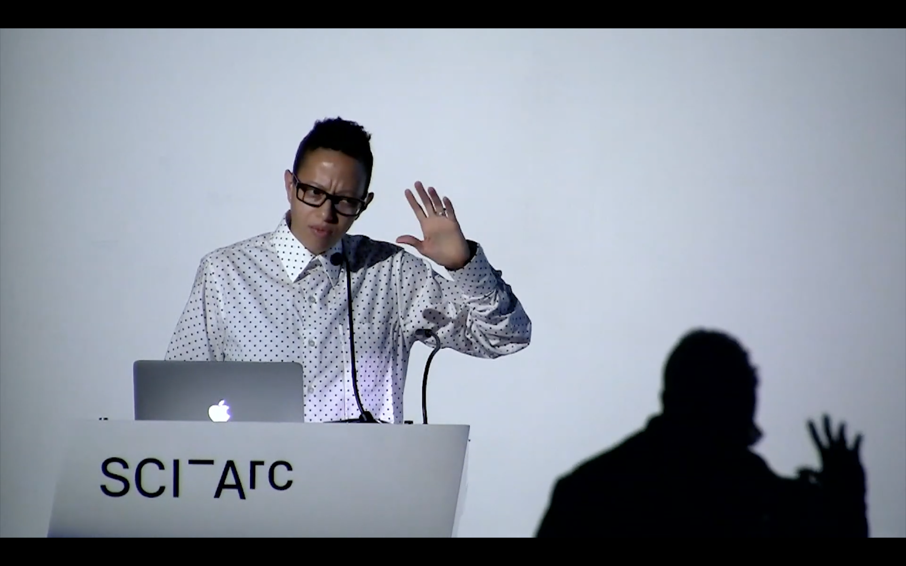 woman speaking from a podium against a white backdrop