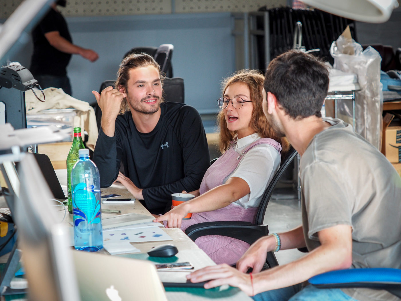 2 male and 1 female graduate students discussing architecture at their desk with computers and desk lamp in school