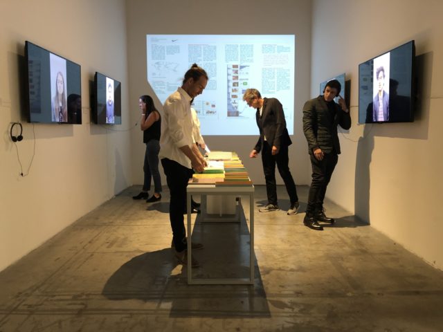 people looking at exhibition with tv screens and books