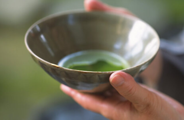 brown ceramic bowl green liquid hands