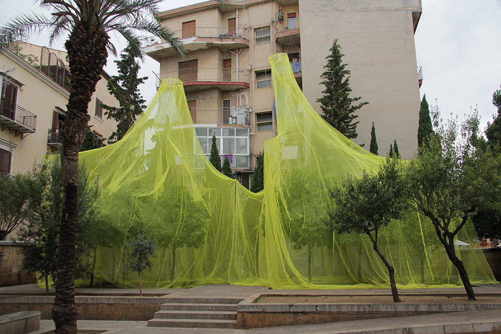 certain trees covered by a huge yellow net suspended from nearby building